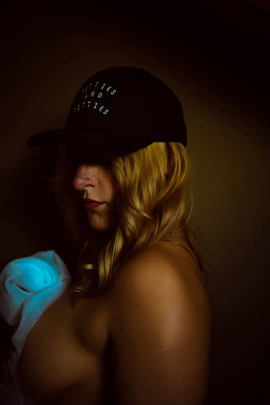 Person wearing a cap with text, holding a glowing blue object against a dark background